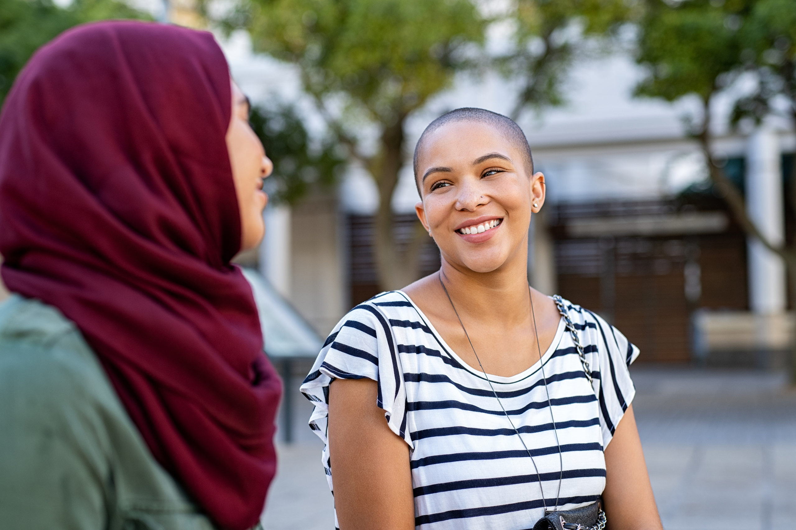 Cheerful african american woman in conversation with muslim girl. Happy multiethnic friends in street looking at each other. Beautiful woman with friend in hijab talking to each others.