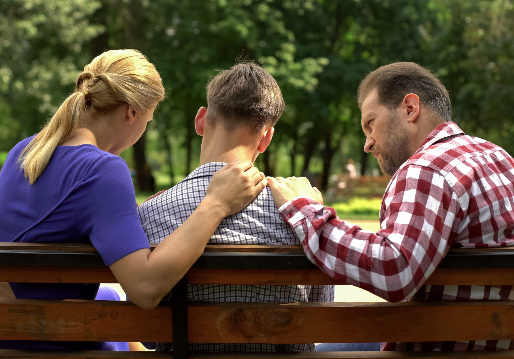 Caring Mother And Dad Supporting Sad Teen Son Sitting On Bench I